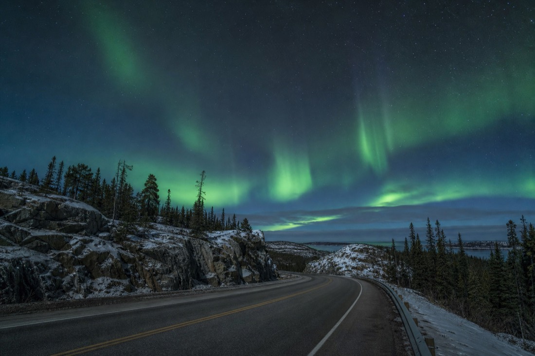 Empty two-lane highway curving between granite outcrops and spruce forest east of Yellowknife
