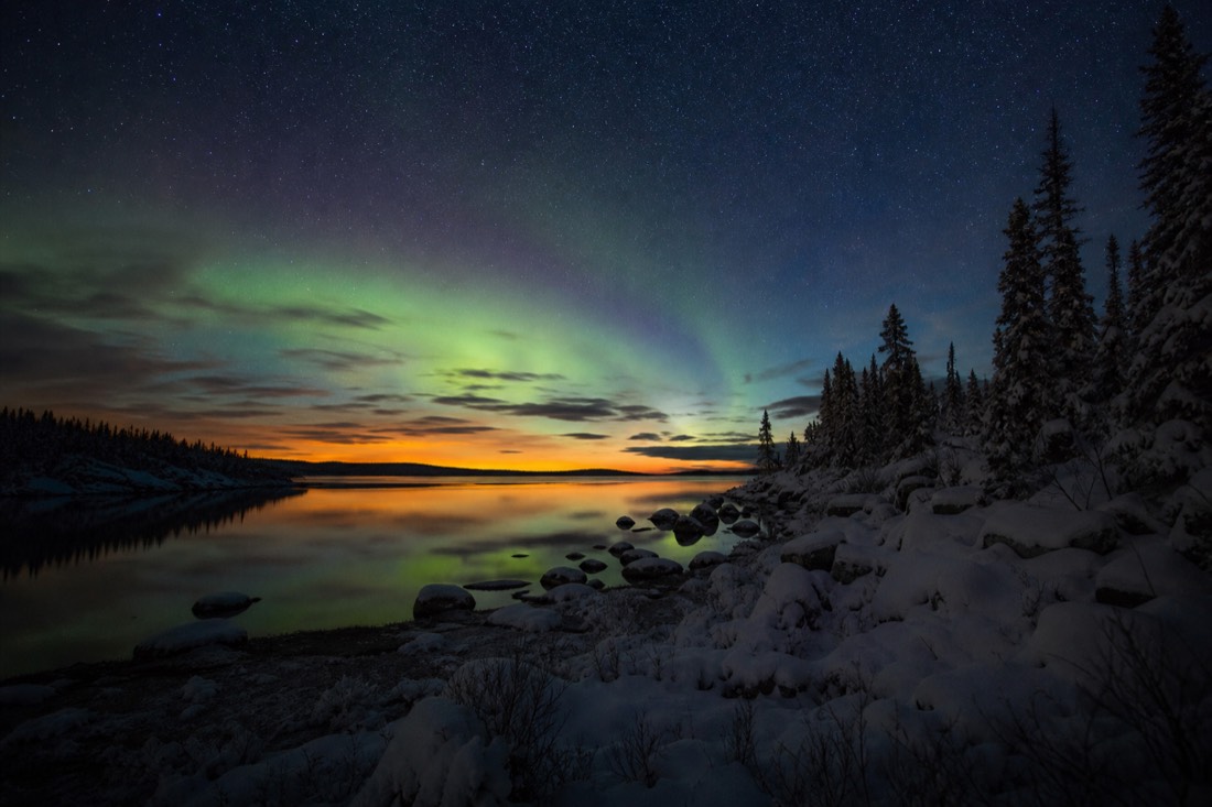 Faint aurora glow above a calm northern lake at night with the last autumn light on the horizon