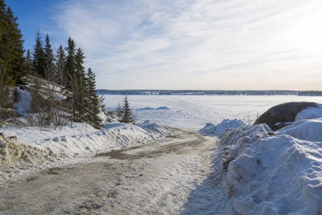 Ice road entrance by the Yellowknife shoreline in March sunshine with snowbanks lining the plowed lane