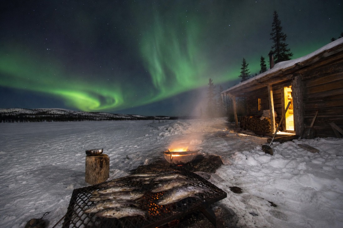 Freshly caught fish cooking outdoors beside a heated hut on a vast frozen lake