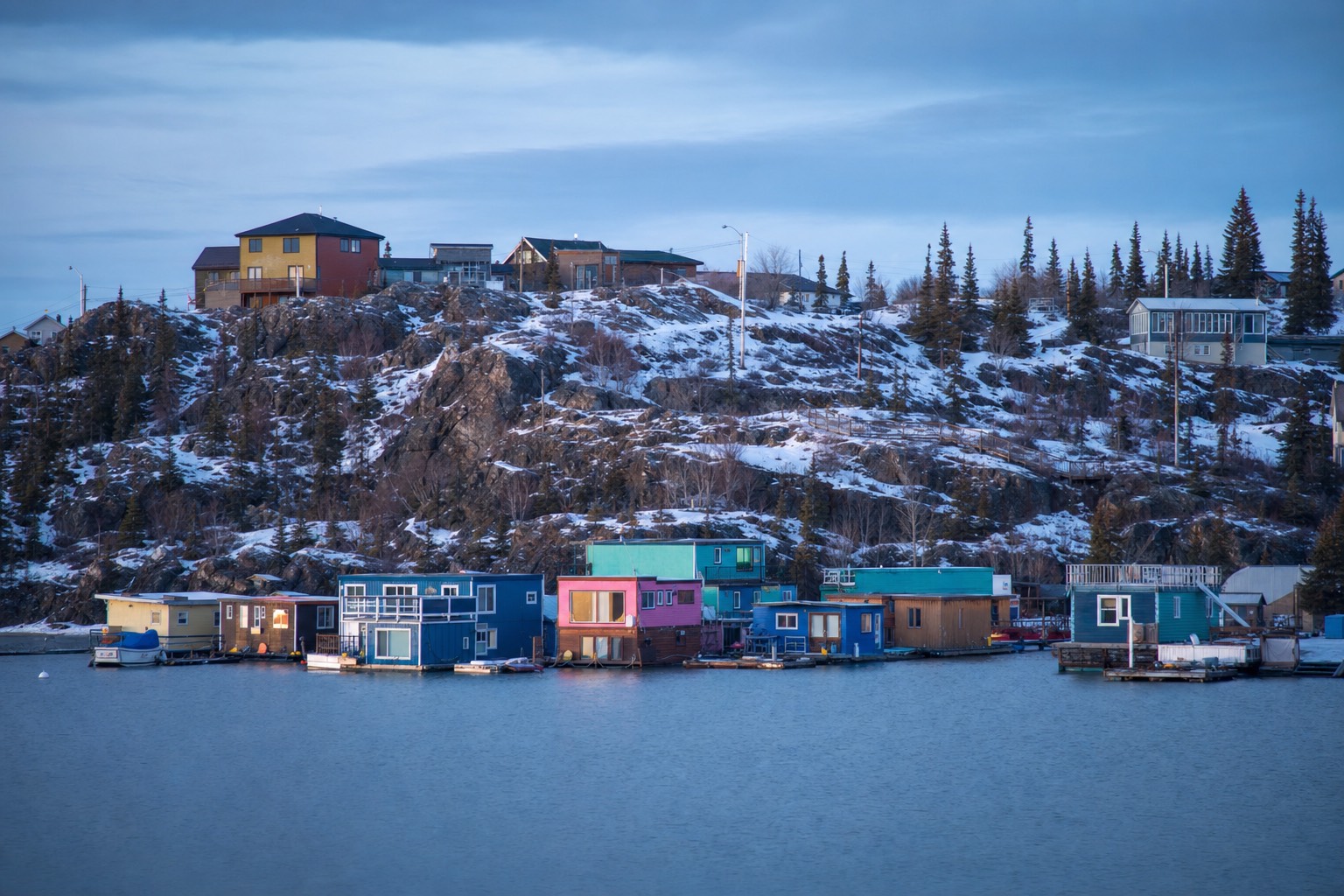 Brightly painted houseboats anchored in Yellowknife Bay on calm summer water below the Old Town rocks