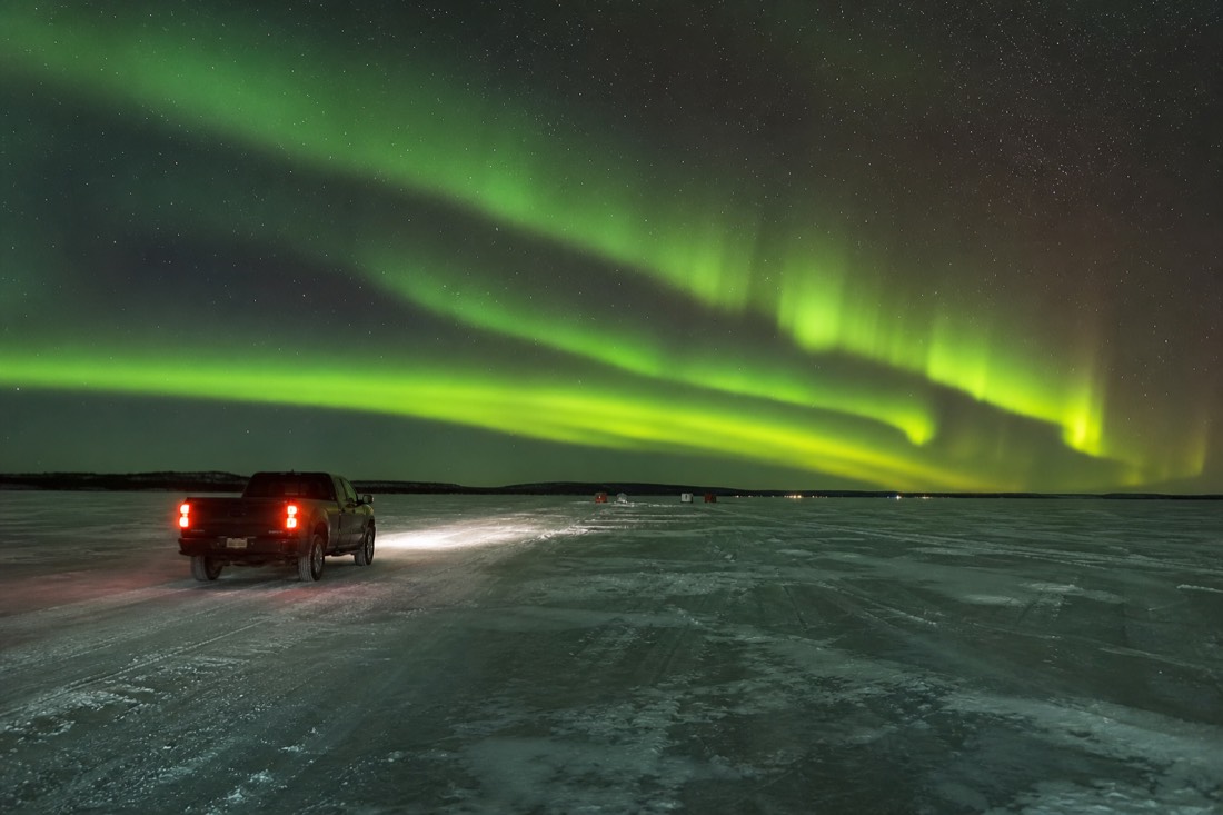 Truck driving across the ploughed ice surface of Great Slave Lake toward distant fishing huts