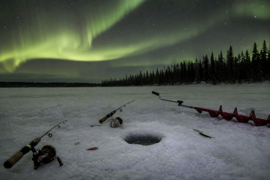 Fishing rods and tackle laid out on the ice beside an auger and a drilled fishing hole
