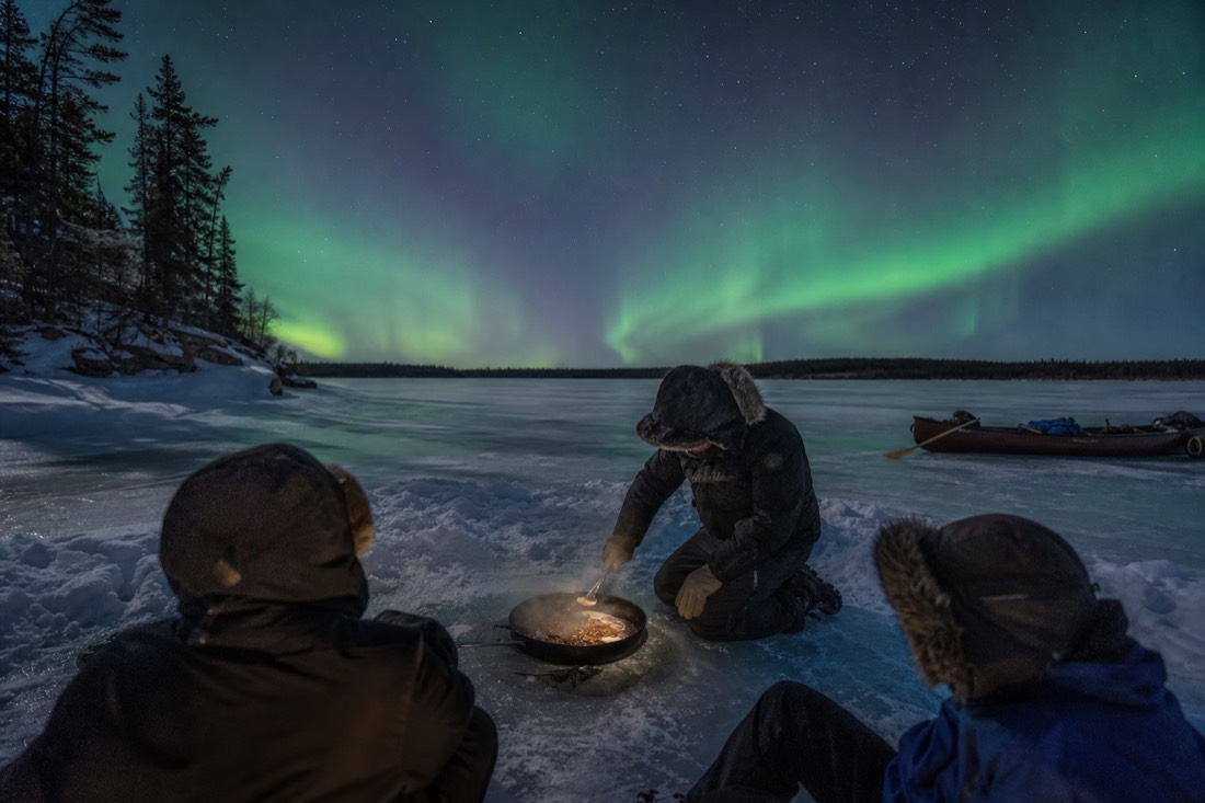 Guide cooking fresh fish in a pan on the ice of Great Slave Lake for a small tour group