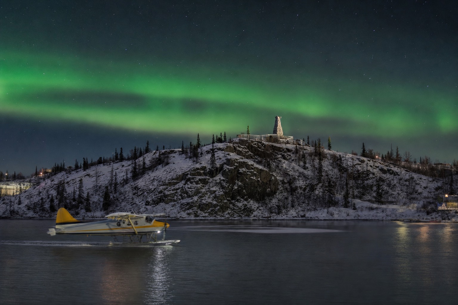 Floatplane taxiing across Yellowknife Bay below the rocky outcrop of the Bush Pilots Monument in Old Town