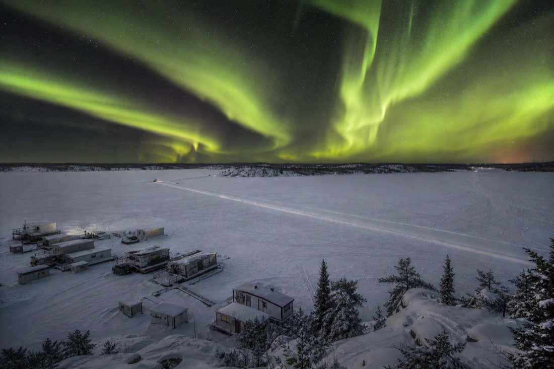 Wide view over frozen Yellowknife Bay with houseboats locked in ice and the Dettah ice road crossing the bay