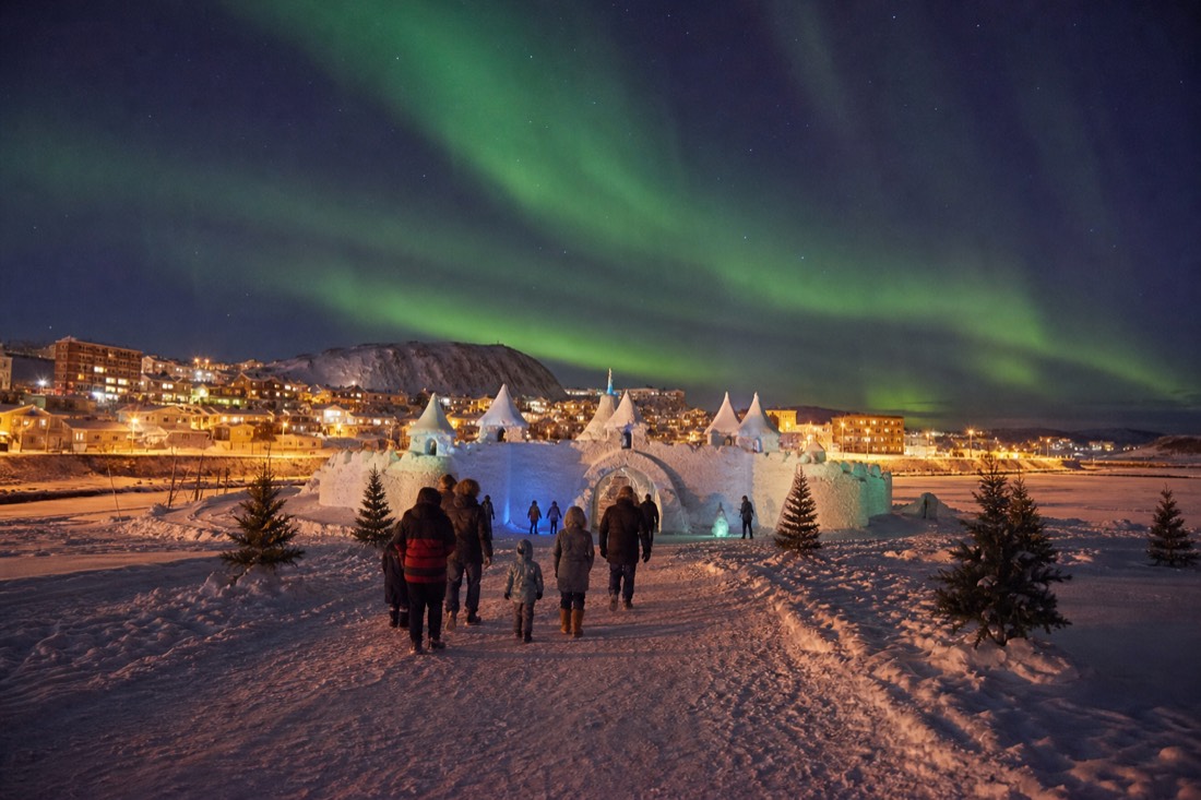 Families walking toward the snow castle entrance on the frozen bay with Old Town on the shore behind