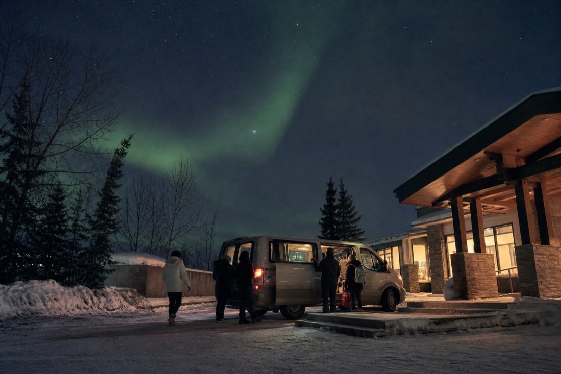 Guests boarding a warm tour van outside a Yellowknife hotel at night in winter