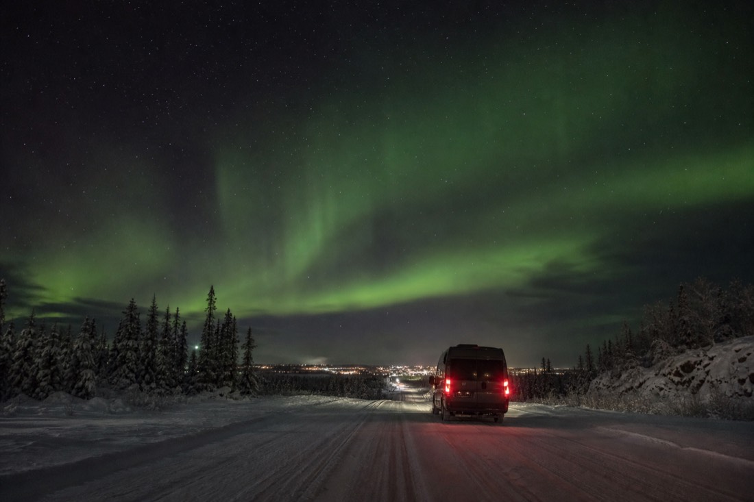 Tour van driving back toward the distant lights of Yellowknife under a starry sky at 2am