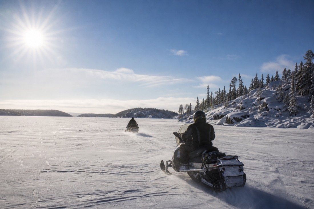 Snowmobiler in full winter gear crossing a frozen lake near Yellowknife in bright cold sunshine