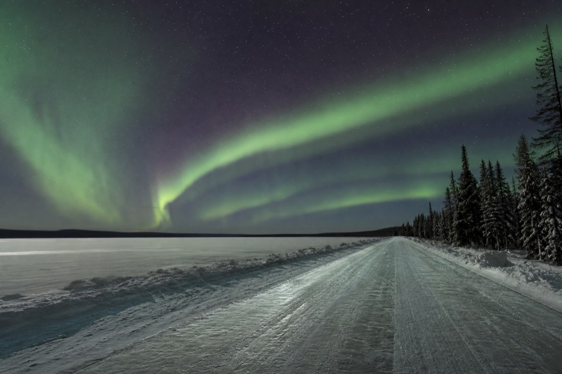Long white ice road stretching to the horizon across a frozen northern lake under low winter sun