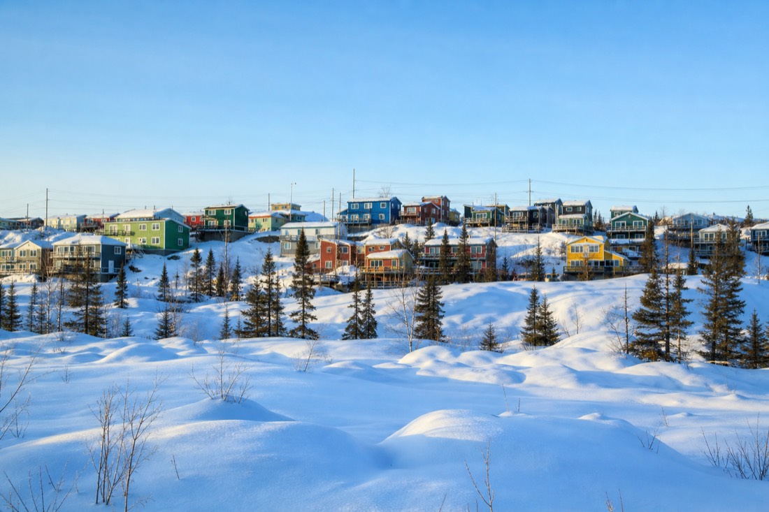 Calm winter afternoon in Yellowknife with colourful houses, deep snow and clear pale blue sky