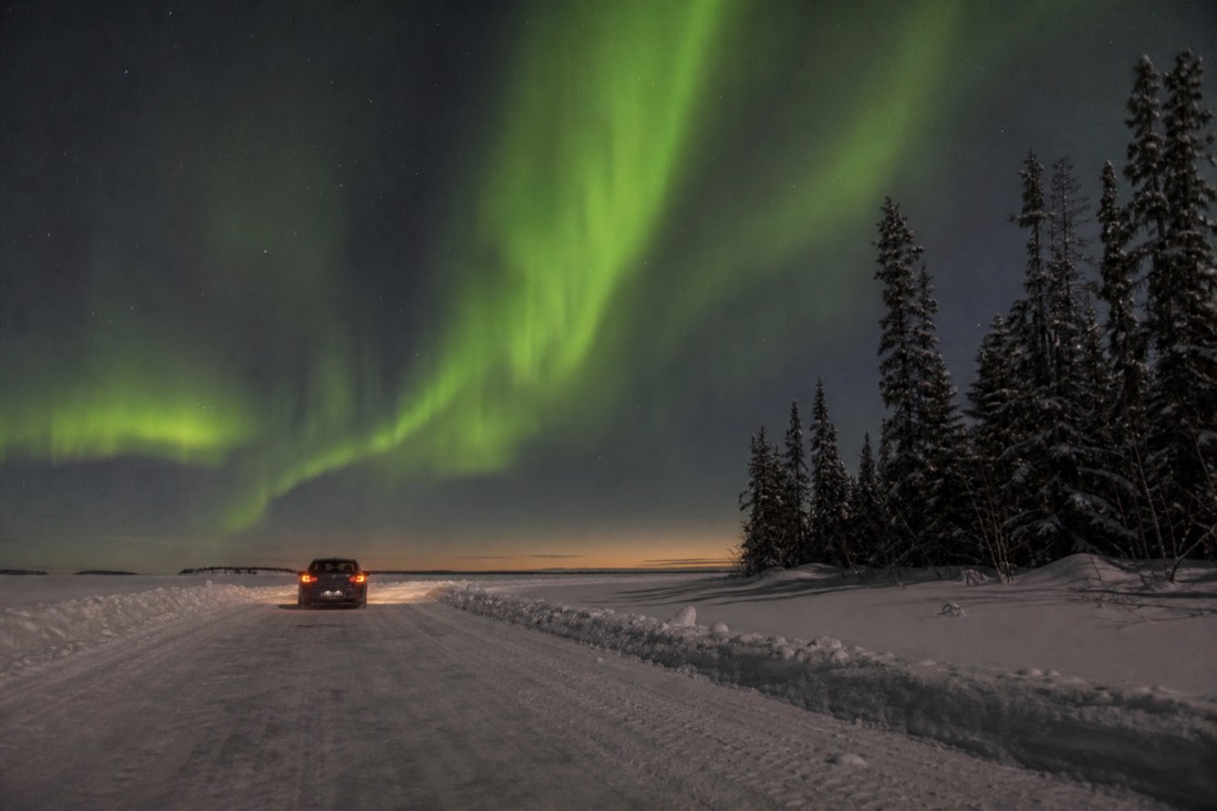 Ordinary car driving the plowed Dettah ice road across frozen Yellowknife Bay with snowbanks marking the lanes