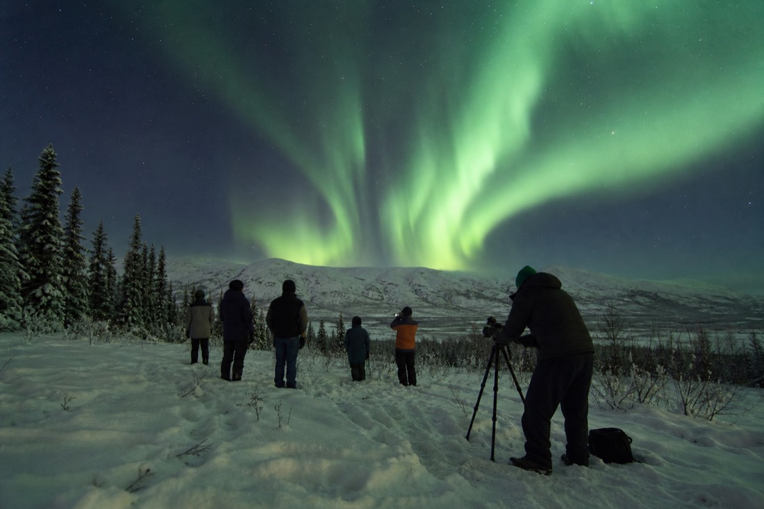 Photographer setting up a tripod for a small tour group beneath bright green aurora curtains