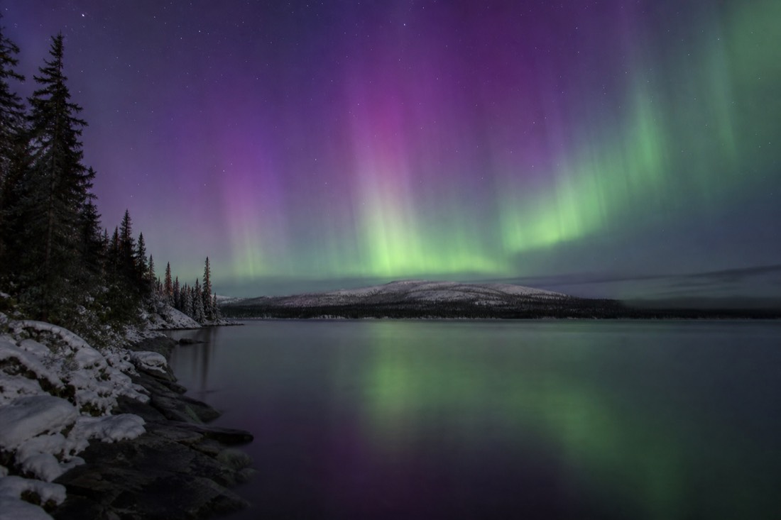 Purple and green aurora reflected in the open water of a northern lake during the autumn season