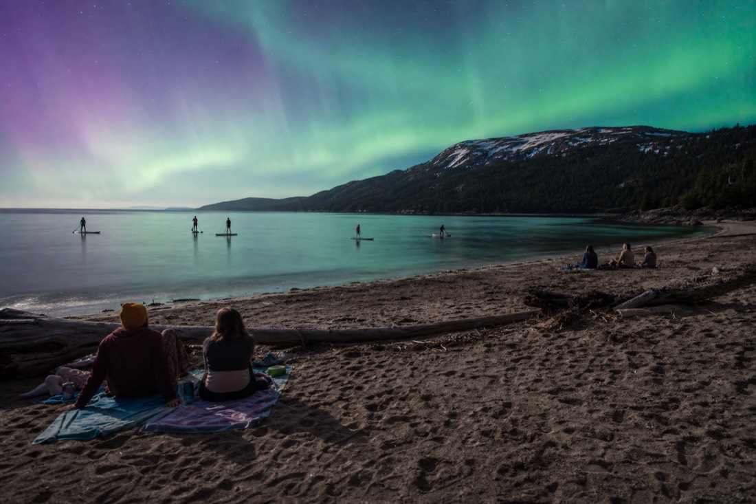 Families on towels along a sandy territorial park beach with paddleboards on calm evening water