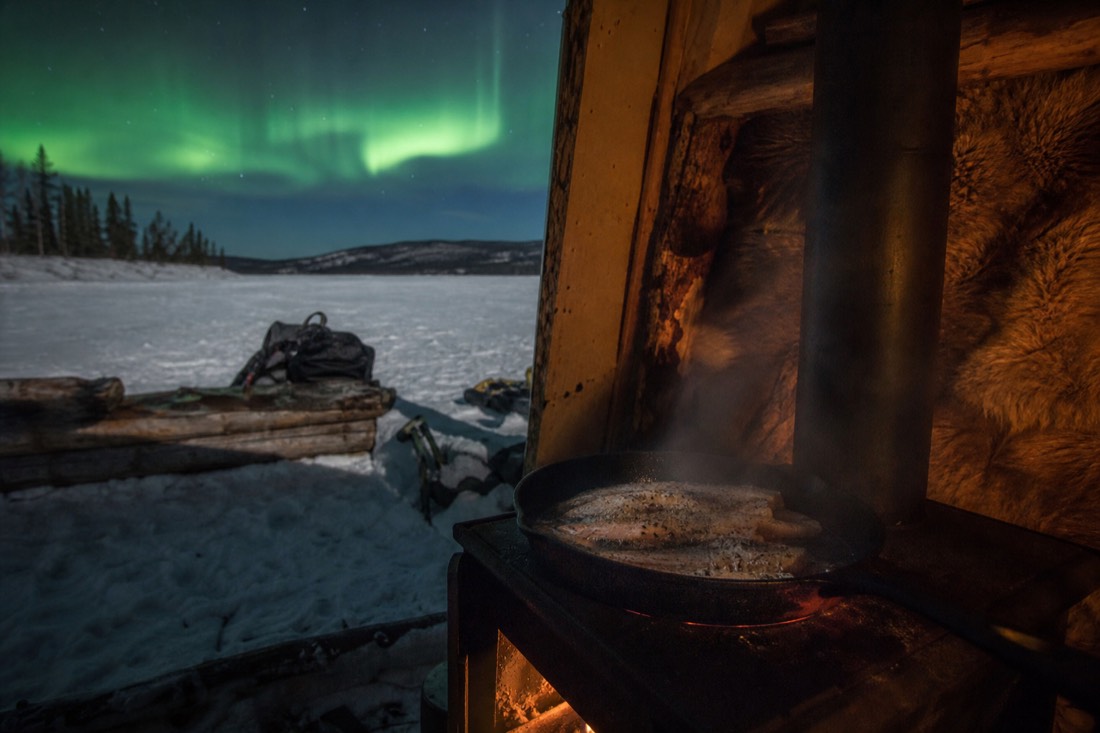 Fresh-caught lake fish sizzling in a pan inside a warm hut on the frozen lake