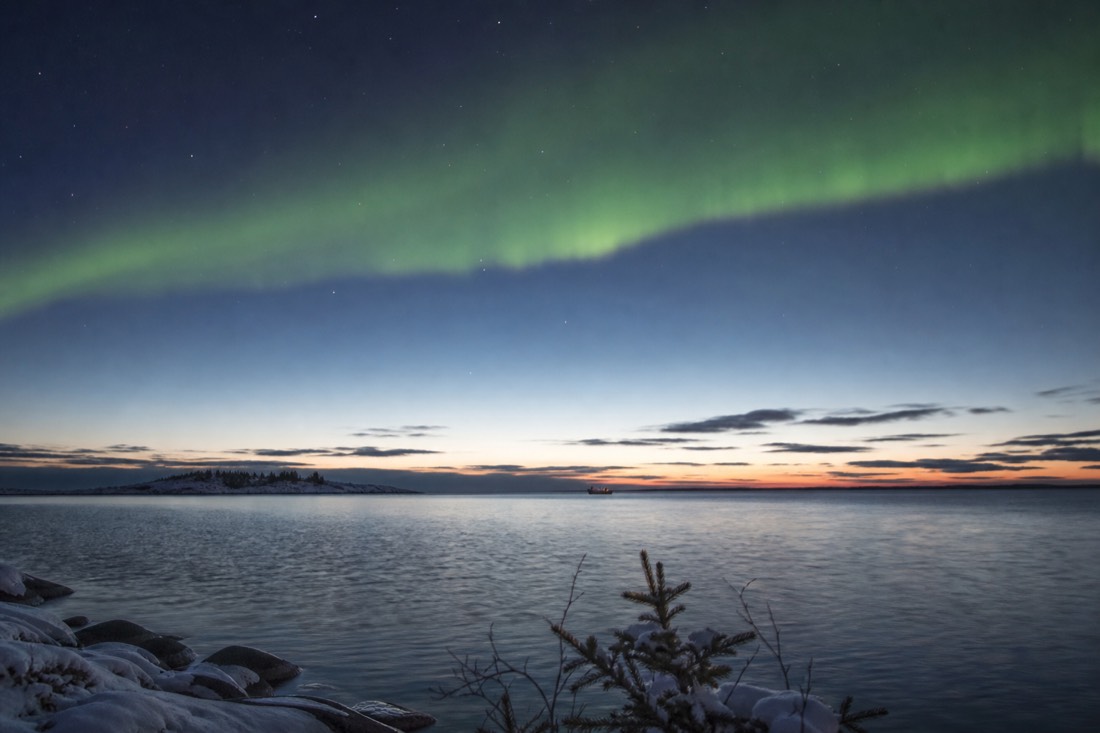 Vast open water of Great Slave Lake at dusk with a tiny boat on the horizon under a huge sky