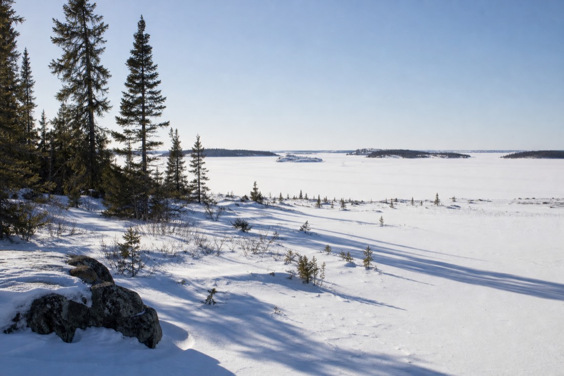 Bright March afternoon on frozen Yellowknife Bay with long shadows on the snow and a clear pale blue sky