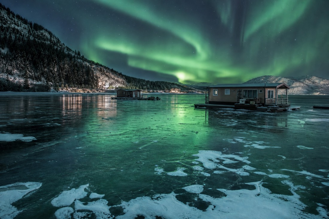 Aurora reflecting on wind-polished lake ice near the Old Town shoreline with houseboats frozen in the bay