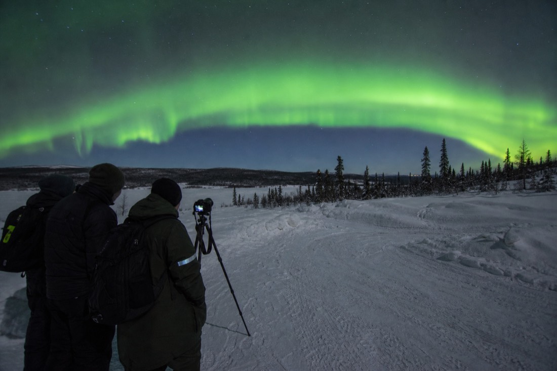 Guests learning camera settings from a guide under a wide green aurora arc on a clear night