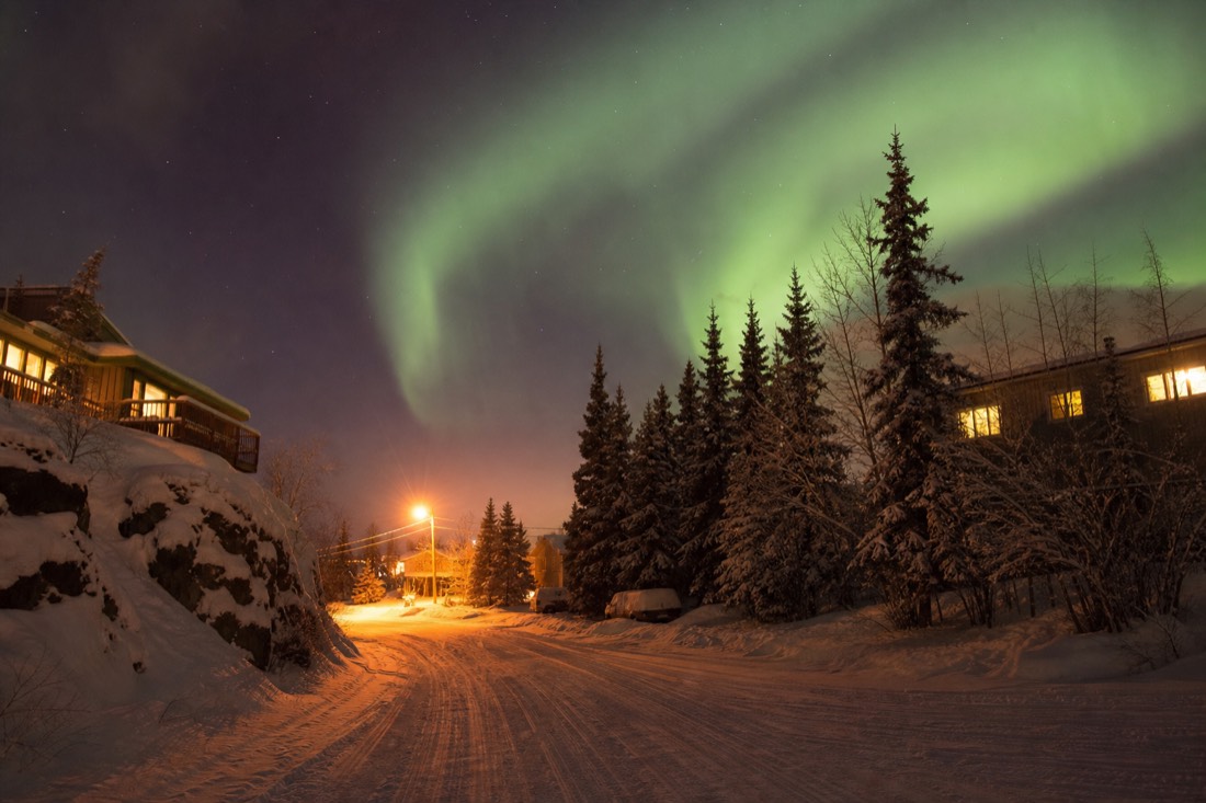 Pink and gold low-angle December light on a snowy Yellowknife street with warm lit windows