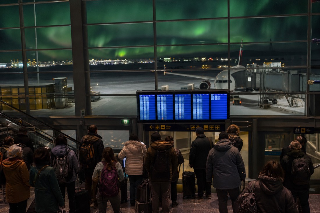 A departures board style scene at a large Canadian hub airport with travelers connecting to a northern flight