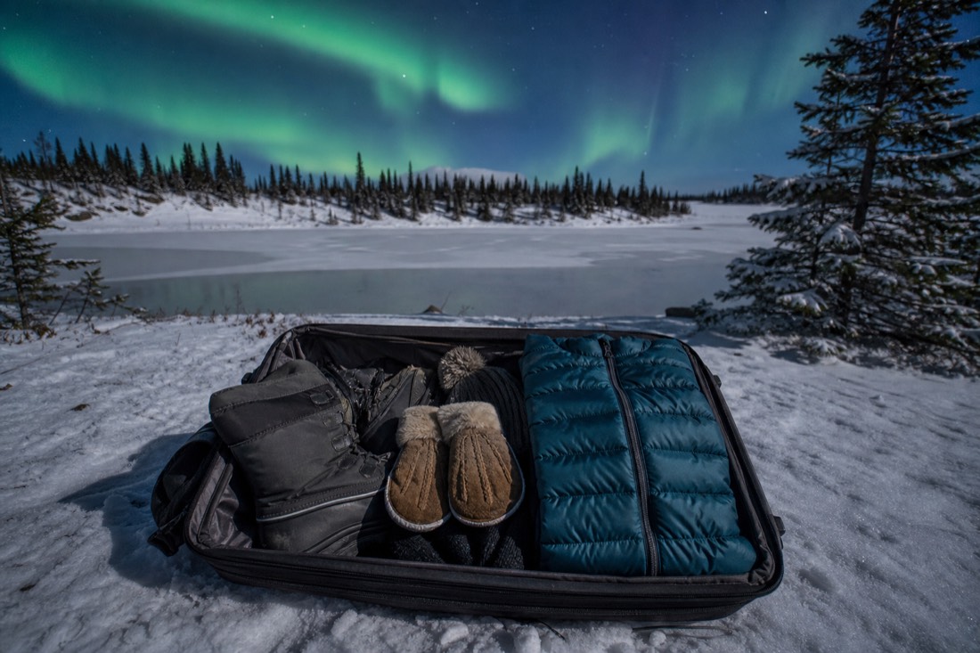 An open carry-on bag packed with a down jacket, mittens, toque and insulated boots ready for an arctic arrival
