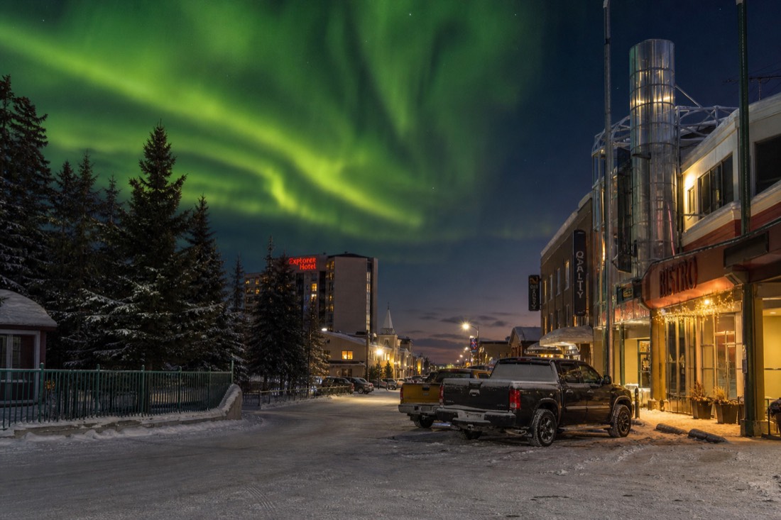 Snowy downtown Yellowknife street at dusk with lit hotel and restaurant signs and parked winter vehicles