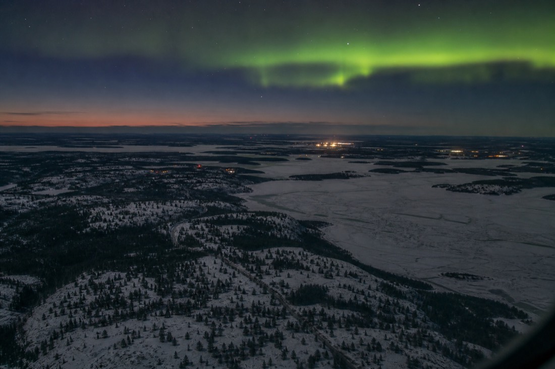 View from an aircraft window of frozen lakes and boreal forest on approach to Yellowknife in winter