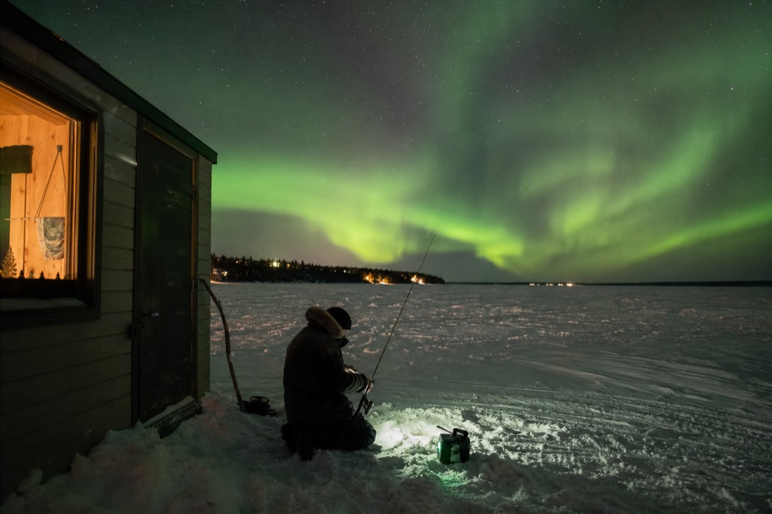 Guide setting up an ice fishing rod outside a heated hut on the vast white surface of Great Slave Lake