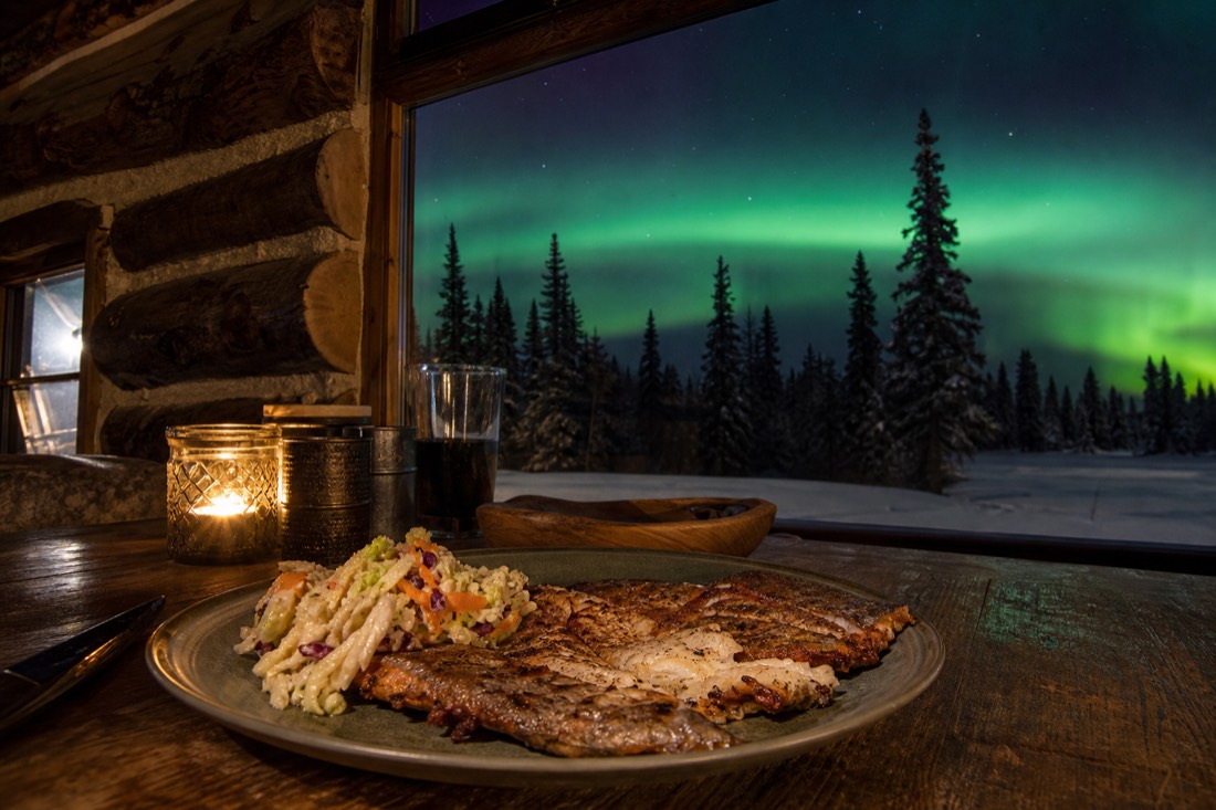 Plate of pan-fried lake fish with sides on a rustic wooden table in a cosy log building