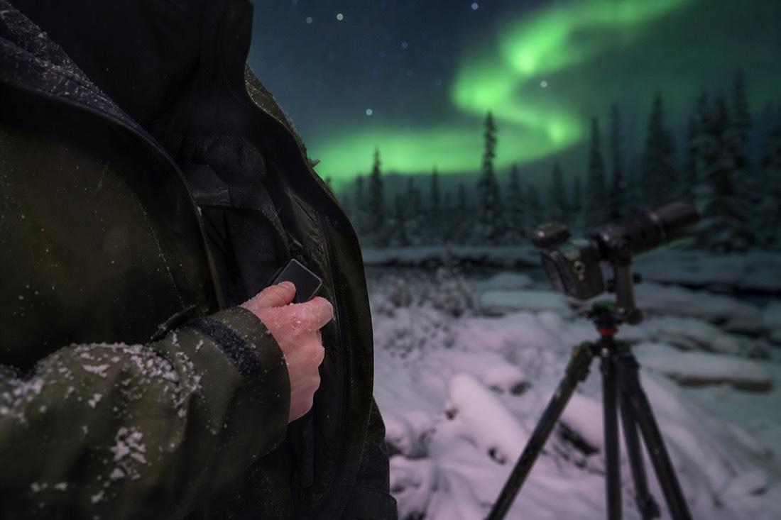 Photographer pulling a spare camera battery from an inner parka pocket on a frigid night shoot
