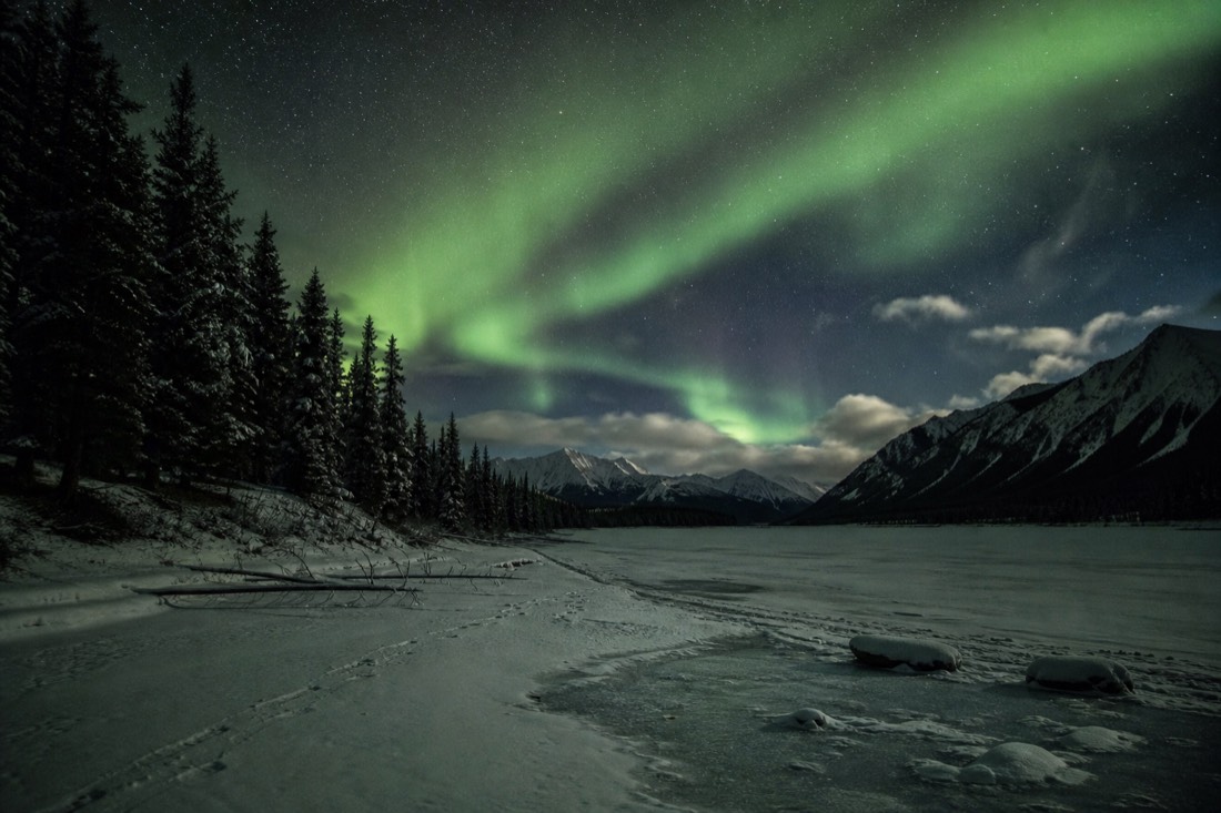 Camera locked on a tripod running a long unattended time-lapse sequence beneath drifting green aurora on a frozen lake