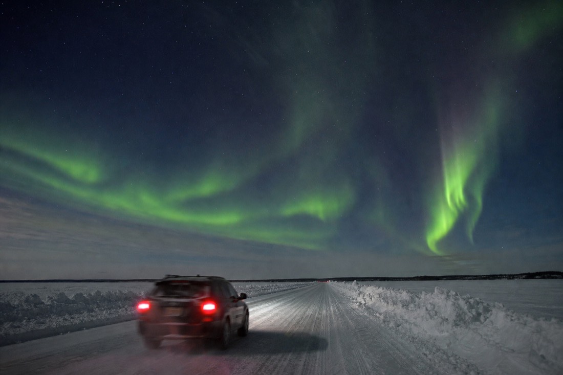 A car driving the marked Dettah ice road across frozen Great Slave Lake with snowbanks lining the route