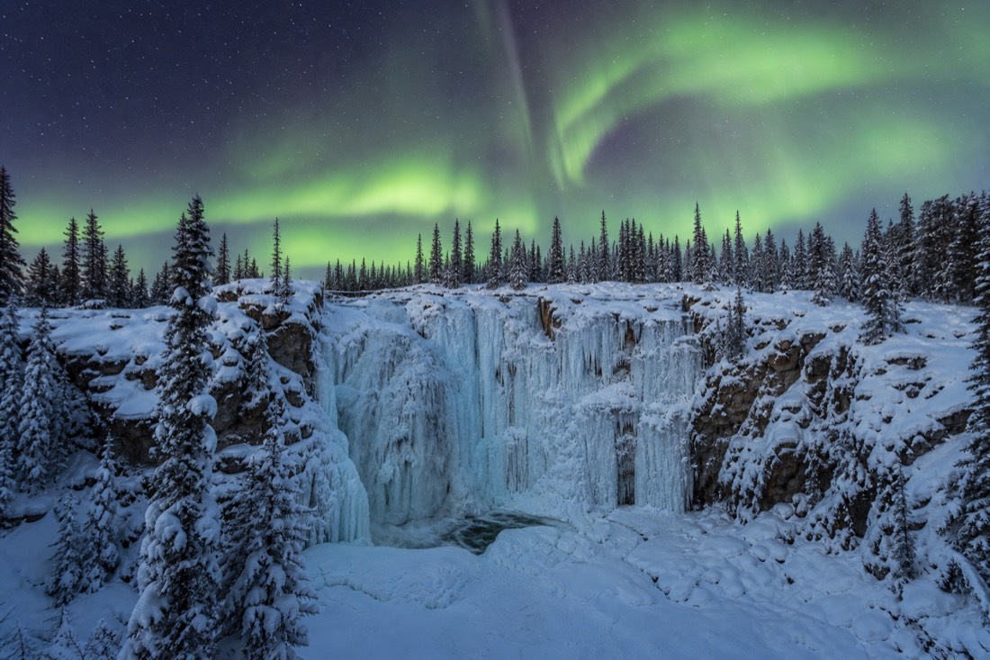 Cameron Falls frozen into blue-white ice columns surrounded by snow-covered spruce forest near Yellowknife