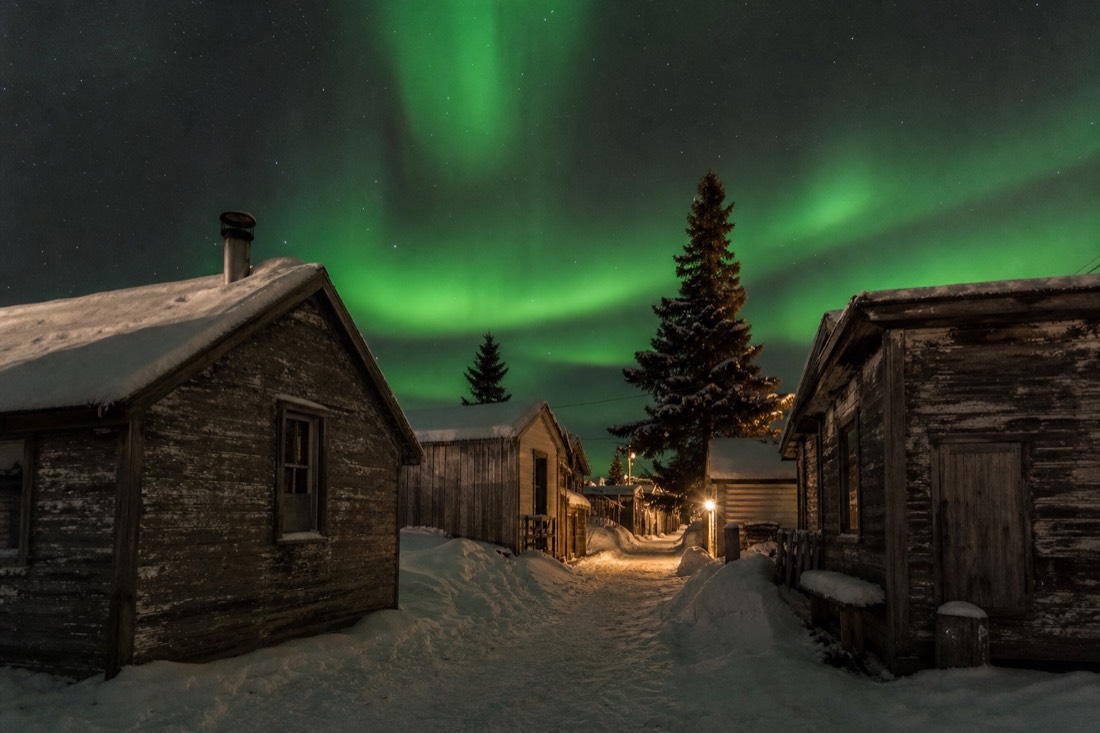 Weathered wooden gold-rush cabins with snow on the roofs along a narrow Old Town Yellowknife lane