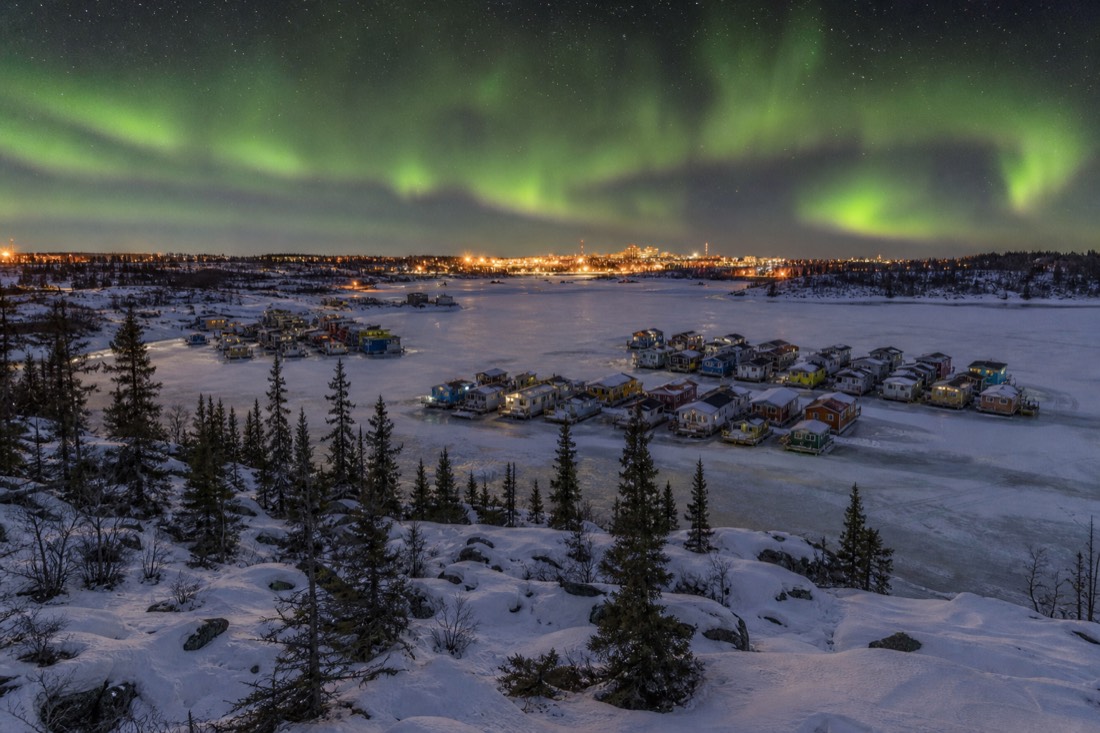 View from the Bush Pilots Monument over colourful houseboats frozen into Yellowknife Bay at golden hour
