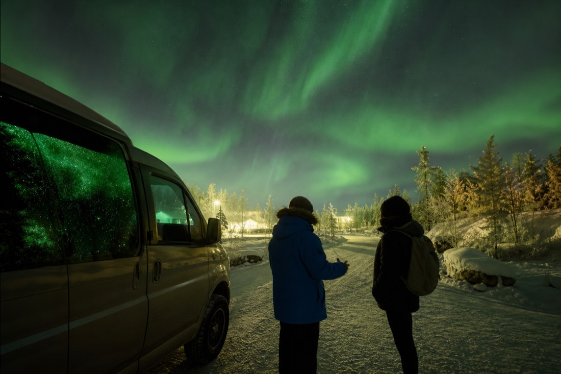 Traveler chatting with a parka-wearing guide beside a tour van on a snowy Yellowknife street