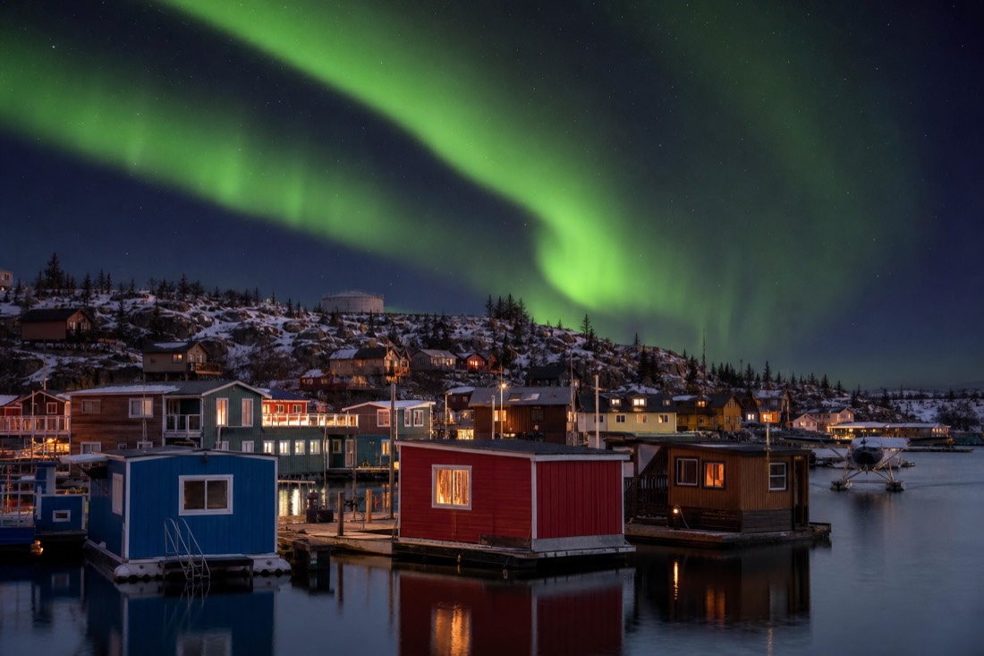 Colourful houseboats moored in Yellowknife Bay with Old Town cabins and a floatplane dock behind