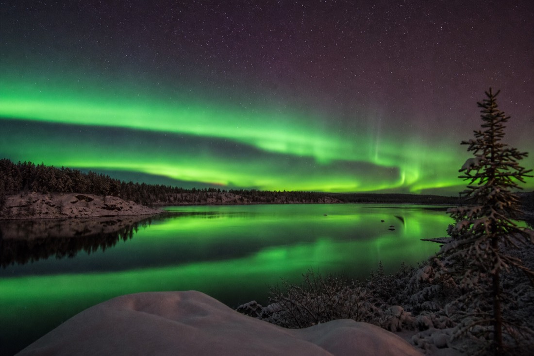 Wide green aurora band reflected in the open water of a lake near Yellowknife in early autumn