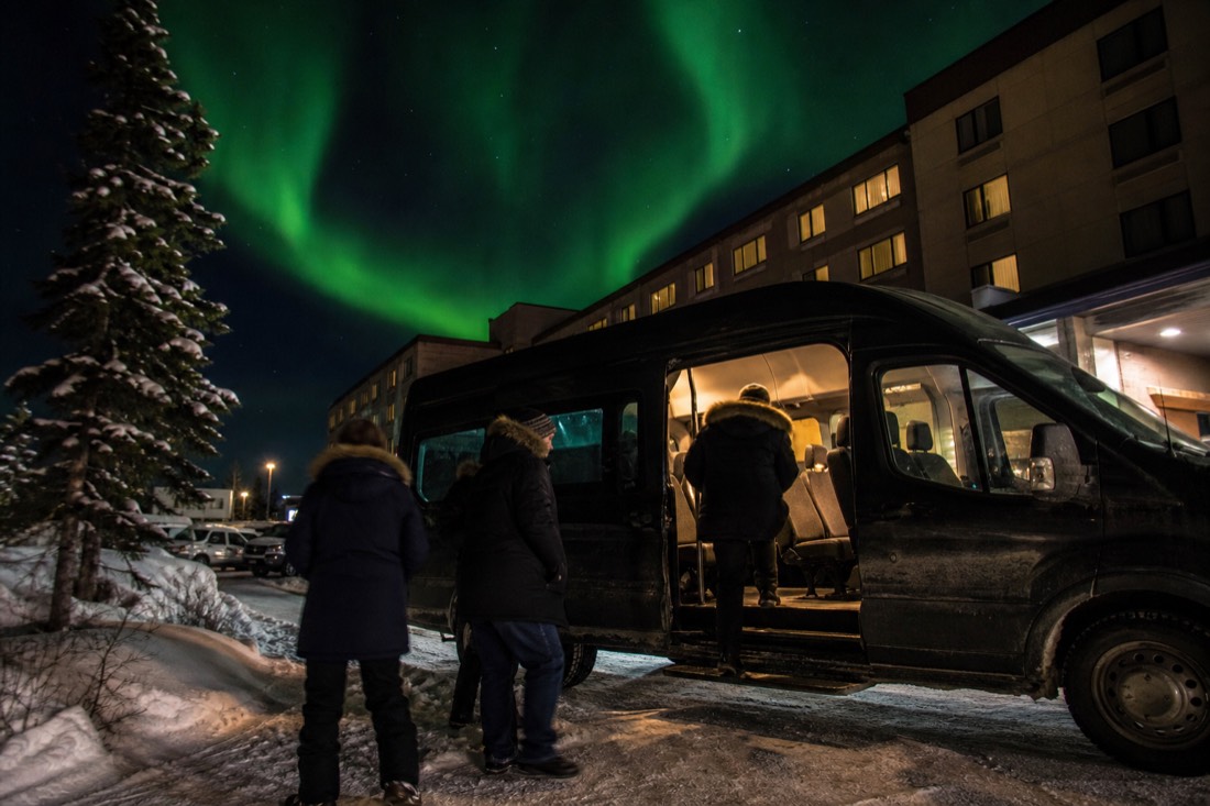 Guests in rented parkas boarding a heated tour van outside a downtown Yellowknife hotel at night