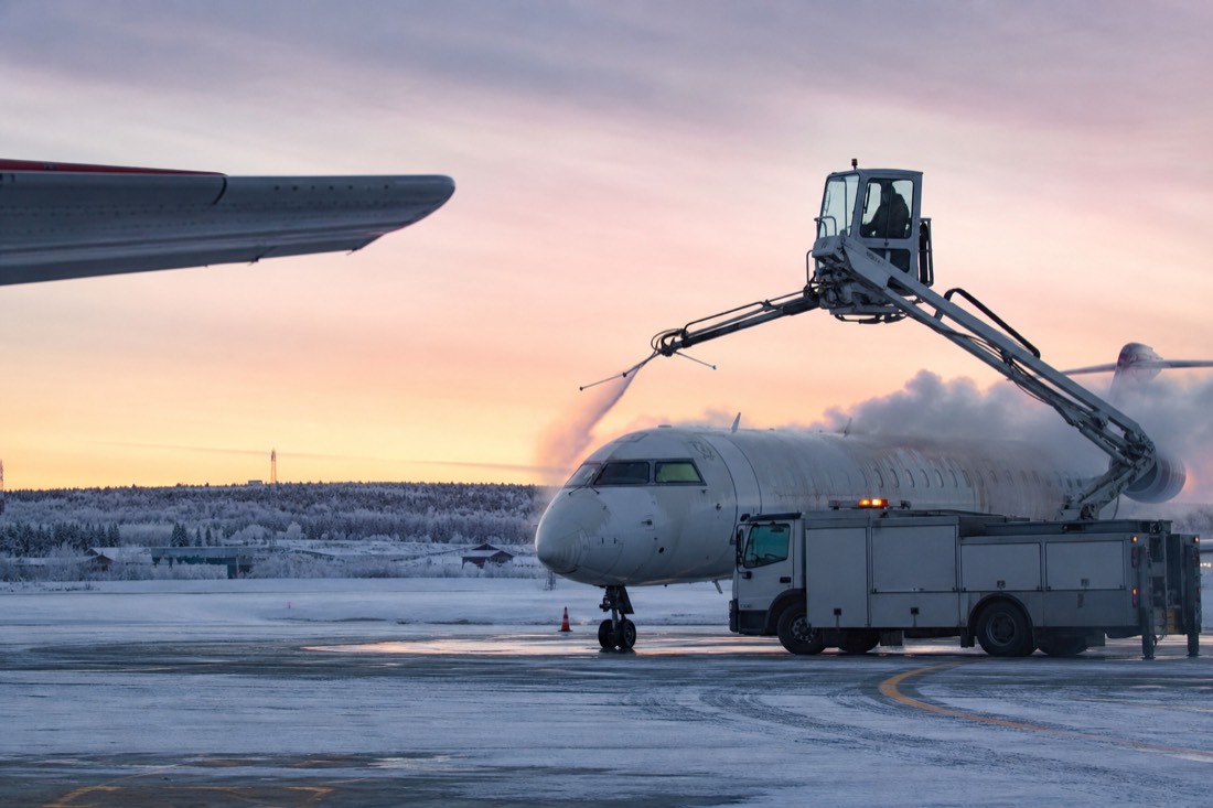 Ground crew de-icing a regional jet on a snowy apron at a northern airport in low pink winter light