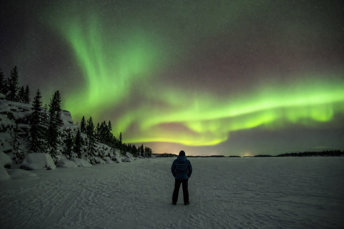 Traveler watching a bright green aurora display from a frozen lake on the third night of a Yellowknife trip