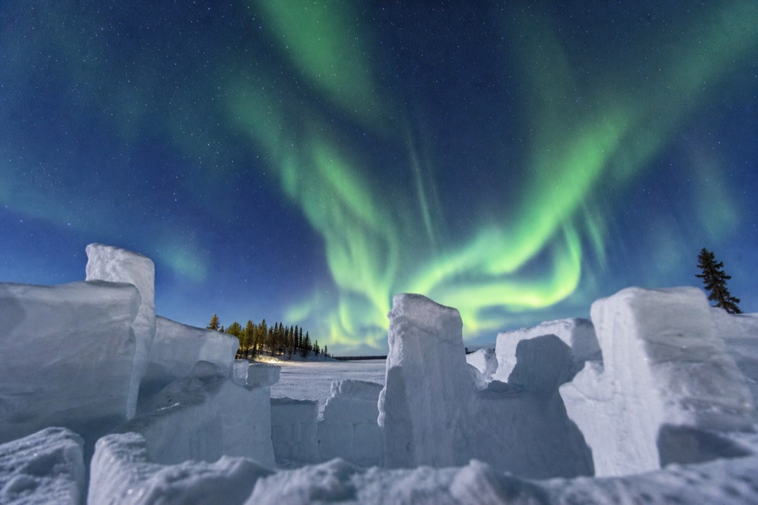 Carved snow castle walls rising from the frozen surface of Yellowknife Bay under a clear blue sky