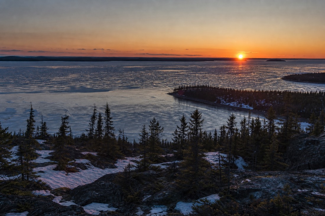 Sun hanging low over Great Slave Lake near midnight in June with the sky still glowing orange