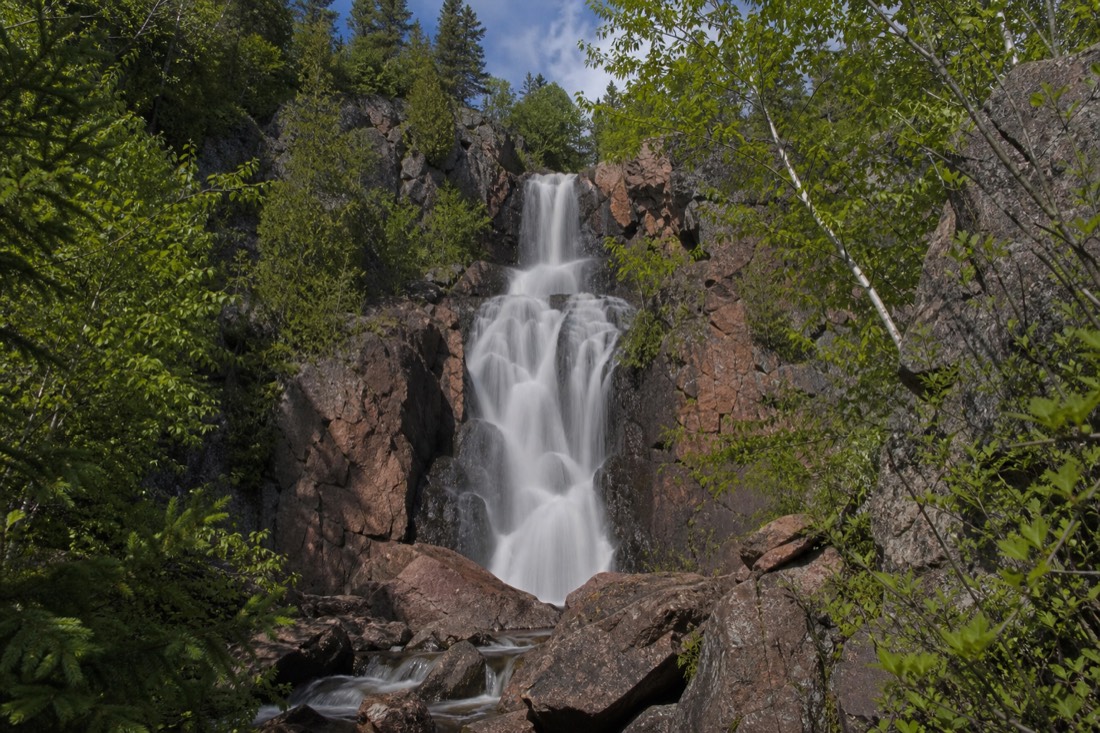 Cameron Falls pouring over pink Canadian Shield rock framed by spruce and birch in full summer green