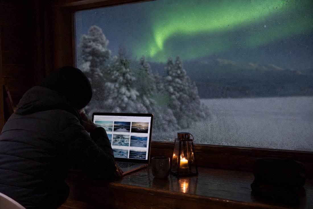 Traveler comparing tour options on a laptop beside a frosted window with snow falling outside