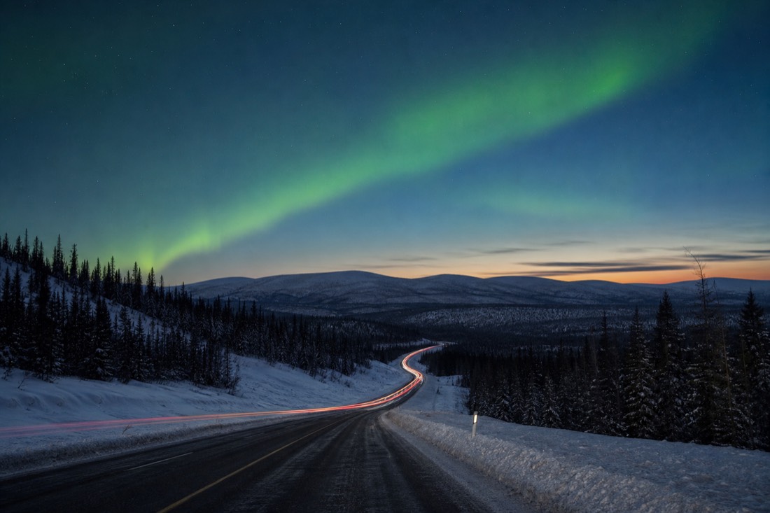 A winter highway running through rolling boreal hills under a pale blue northern dusk