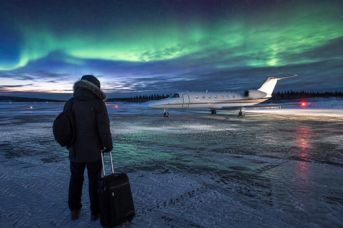 Traveler with a suitcase watching a small jet on a snowy northern airport apron at twilight